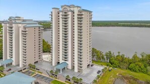 A high-rise residential building with multiple balconies, a parking area, and a view of a large body of water. - Trendy Lake Condo-Disney view! (Orlando)