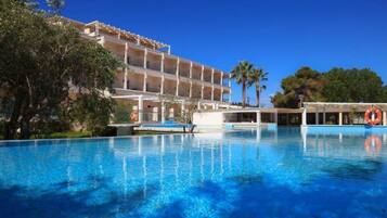 A hotel with a large swimming pool, a covered outdoor area, and a multi-story building with balconies.