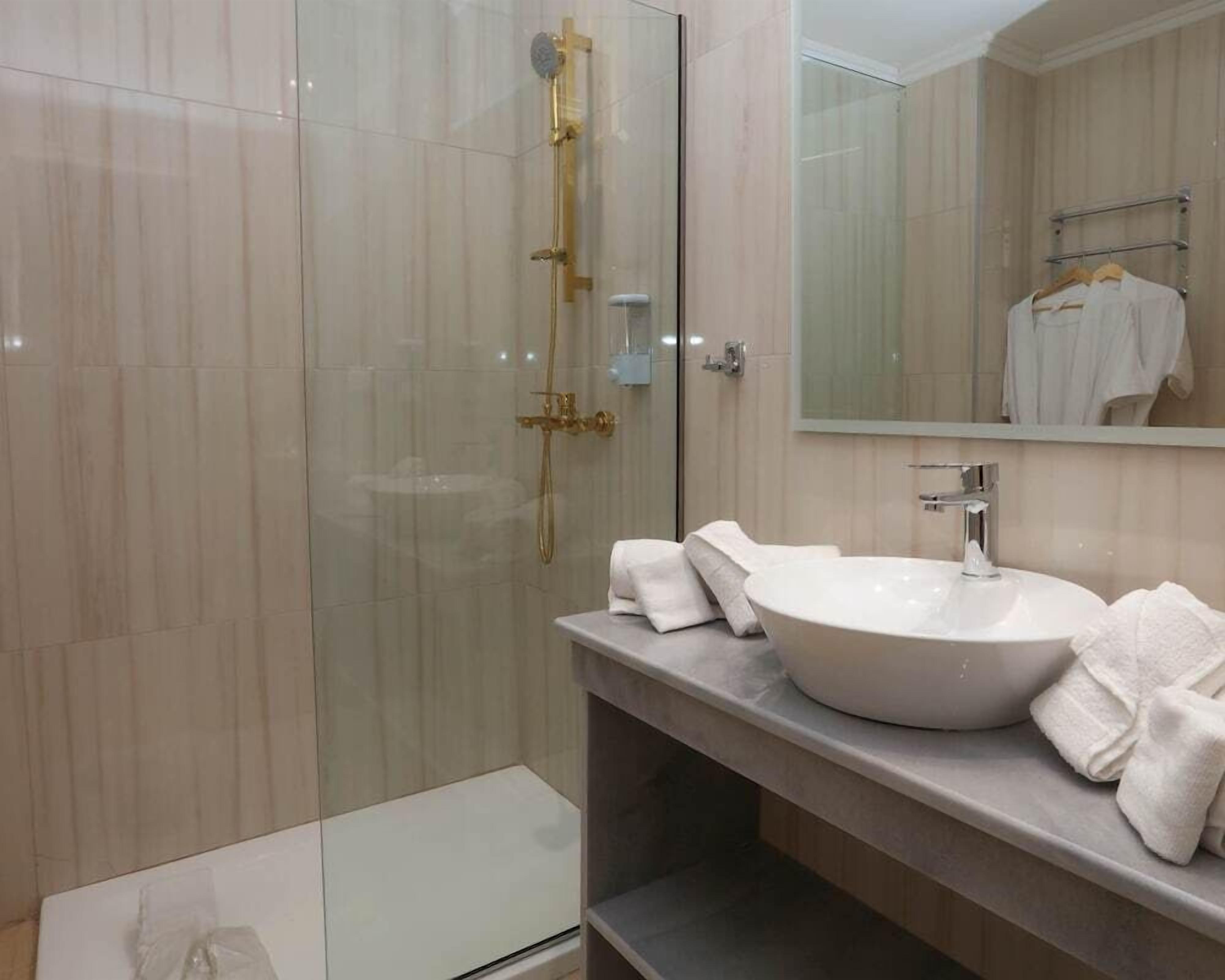Un baño moderno con ducha acristalada, lavamanos blanco y espejo sobre el mueble-lavabo.