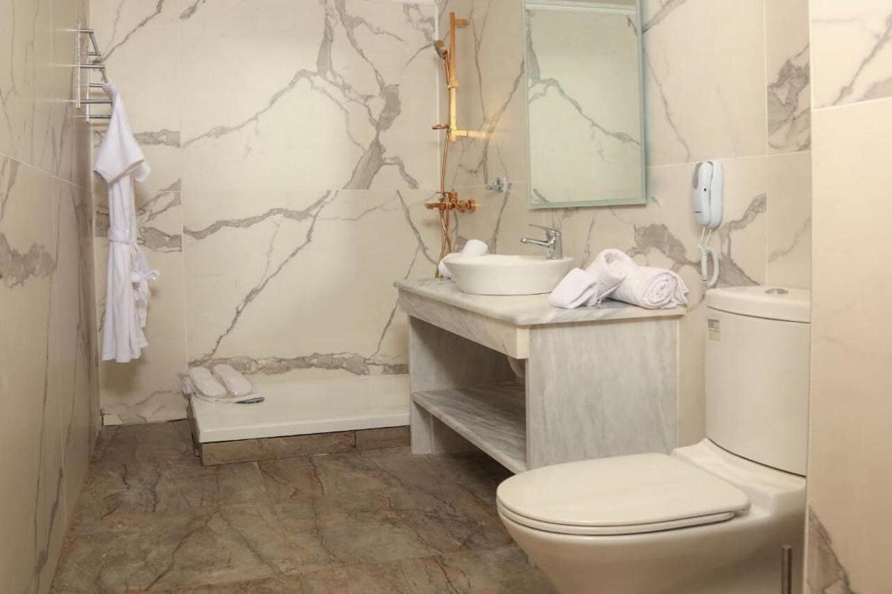 Un baño con pared de mármol, una bañera, un lavabo, un inodoro y un perchero para toallas.