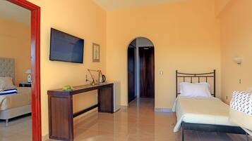 A hotel room with a bed, a desk, a television, and a door leading to another room.