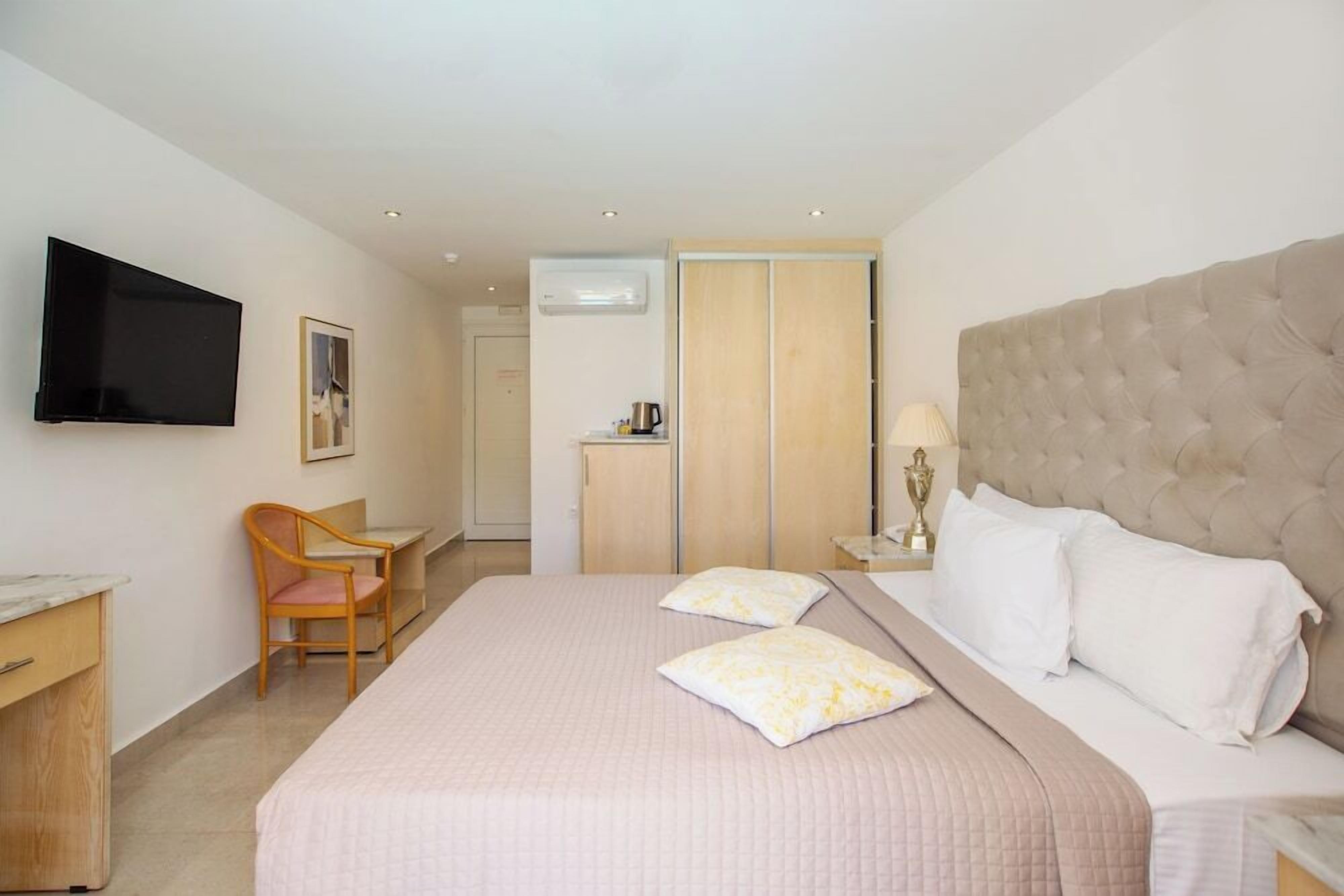 A hotel room with a bed, a desk, a chair, a TV, and a wardrobe.