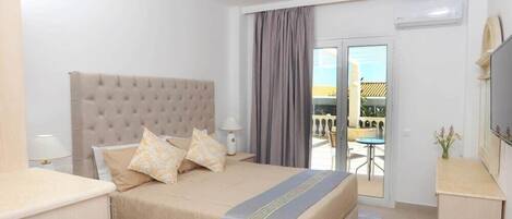 Habitación de hotel con una cama grande, televisión, balcón con mesa y sillas, y aire acondicionado.