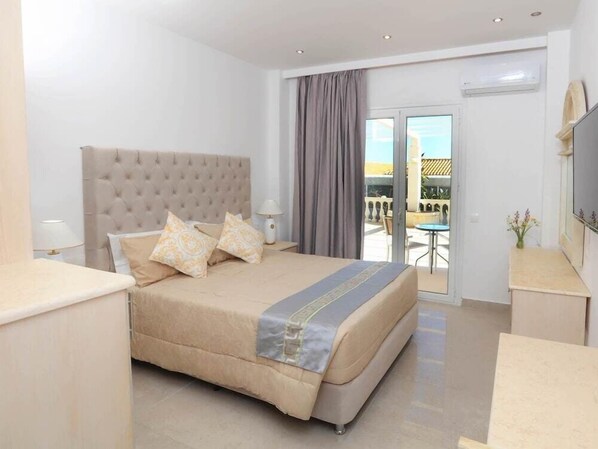 Habitación de hotel con una cama grande, televisión, balcón con mesa y sillas, y aire acondicionado.