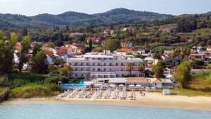 Un hôtel situé sur la côte, avec plusieurs étages, une plage équipée de transats et un espace piscine.