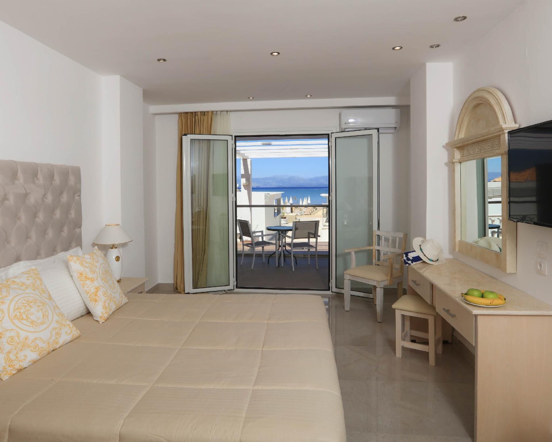 Una camera d'albergo con un letto, una scrivania, una sedia, una TV e un balcone vista mare.