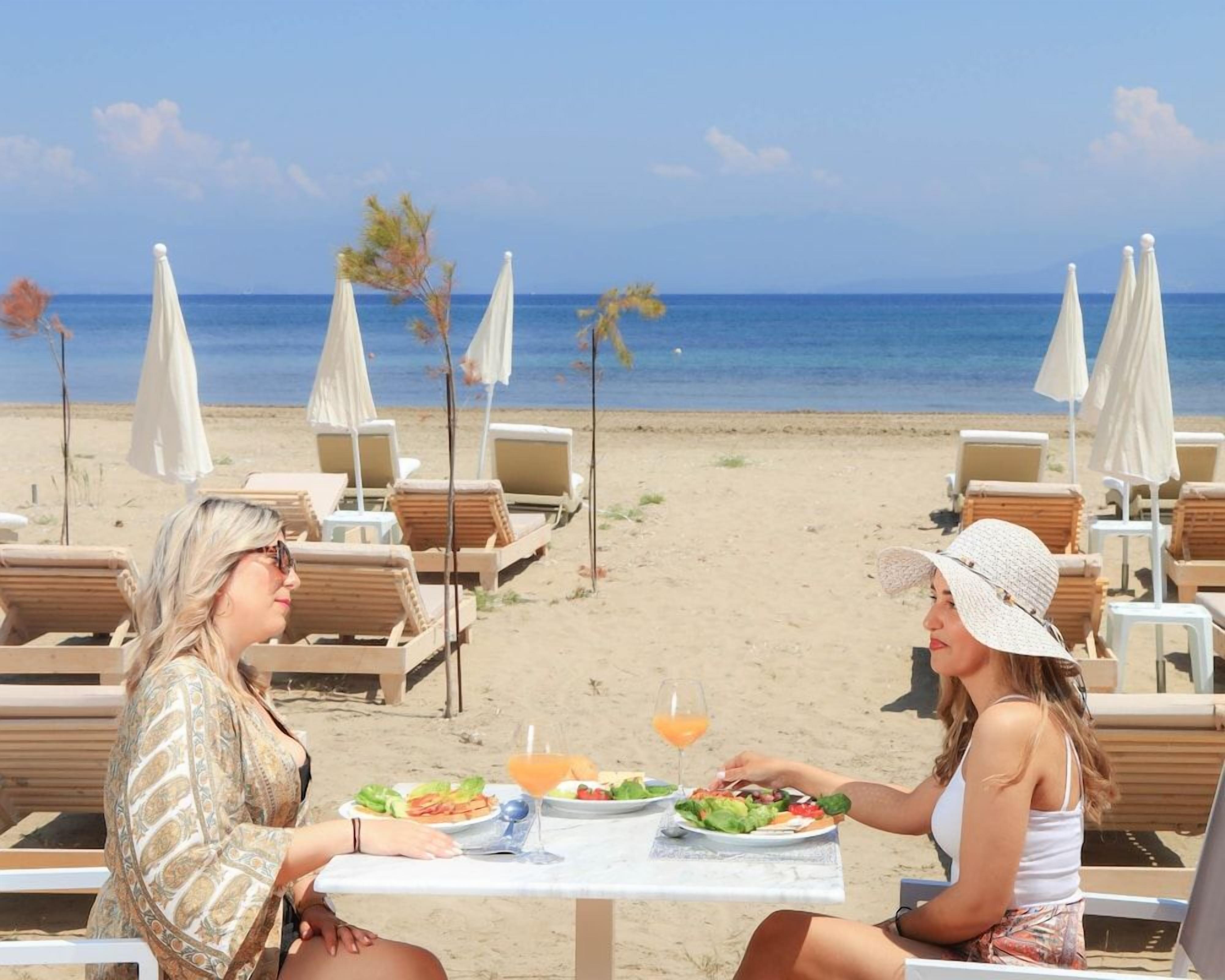 Un área de comedor en la playa con mesas y sillas, con vista al océano.