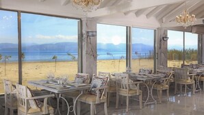 Un espace repas avec des tables préparées pour deux personnes, de grandes fenêtres donnant sur la plage et des lustres.