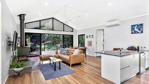 A modern kitchen with a central island, a dining area with a high ceiling, and a living room with a sofa and coffee table.