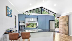 A modern kitchen with a central island, stainless steel appliances, and a view of greenery through a large window.