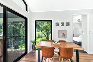 A modern dining area with a large table, leather chairs, and a view of a lush garden through a glass door. - Under the Pecans | 2BR Retreat with Peaceful Scenic Views (Woombye)