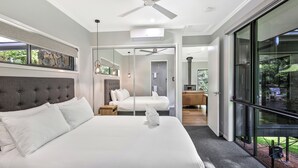 A modern hotel room with a large bed, a ceiling fan, and a view through a glass door.