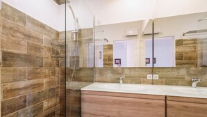Un baño moderno con cabina de ducha de vidrio, tocador de madera y un espejo grande.