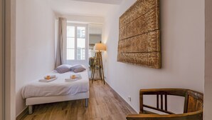 Un dormitorio con una cama, una silla de madera, una lámpara de pie y una obra de arte grande en la pared.