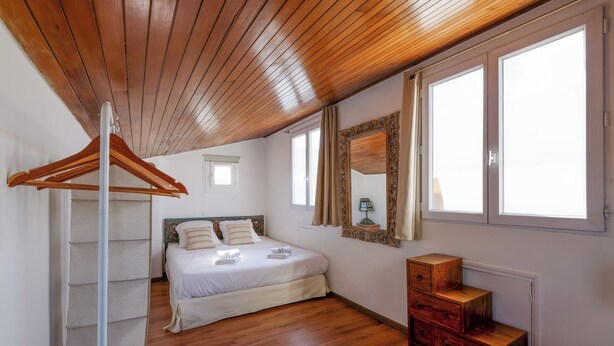 A bedroom with a wooden ceiling, a bed with white linens, a wooden dresser, and a window with curtains. - Appartement Le Bateau Tropézien - Welkeys (Saint-Tropez)