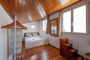 A bedroom with a wooden ceiling, a bed with white linens, a wooden dresser, and a window with curtains. - Appartement Le Bateau Tropézien - Welkeys (Saint-Tropez)