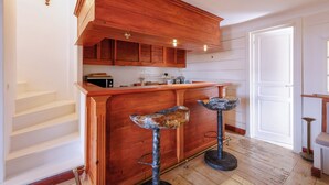 A kitchen with wooden cabinets, a bar area with stools, and a staircase. - Appartement Le Bateau Tropézien - Welkeys (Saint-Tropez)