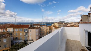 A rooftop terrace with a view of a cityscape, including buildings and distant mountains. - Appartement Le Bateau Tropézien - Welkeys (Saint-Tropez)