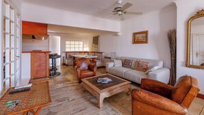 A spacious living room with a wooden coffee table, leather armchairs, a white sofa, and a dining area with a table and chairs. - Appartement Le Bateau Tropézien - Welkeys (Saint-Tropez)