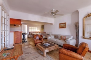 Ein geräumiges Wohnzimmer mit Couchtisch aus Holz, Ledersesseln, einem weißen Sofa und einem Essbereich mit Tisch und Stühlen.