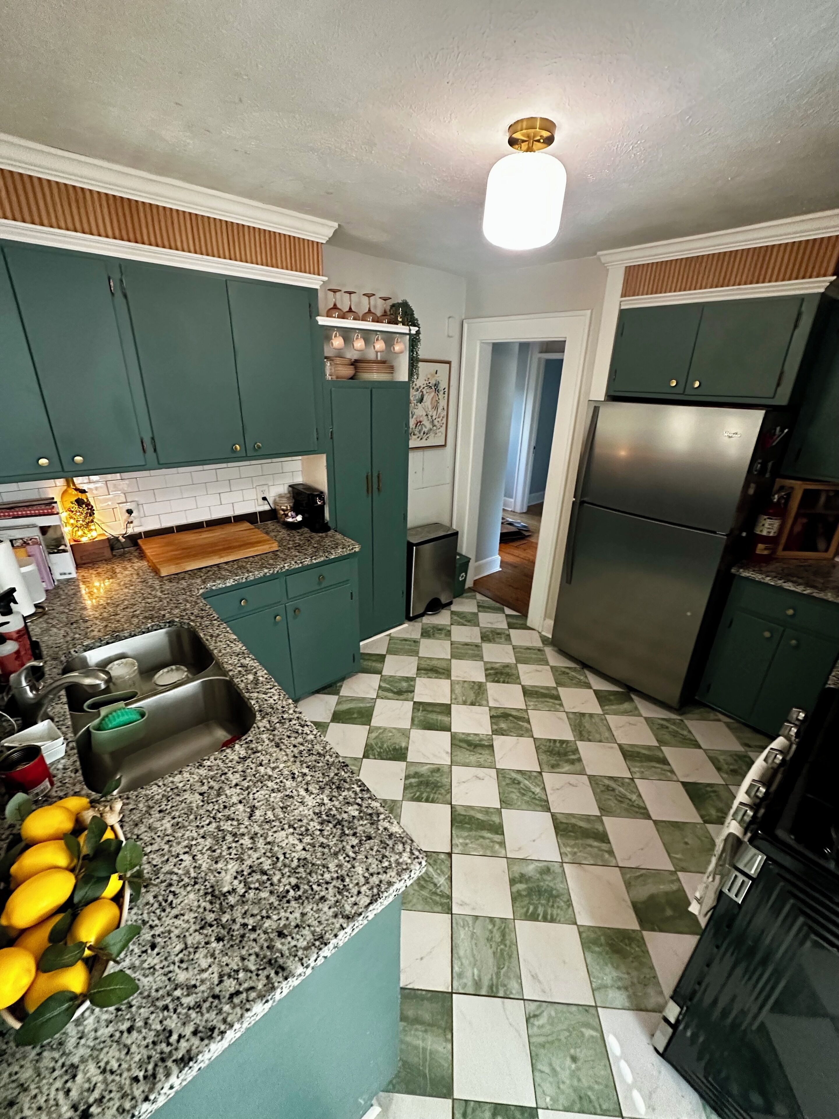 A kitchen with teal cabinets, a checkered floor, a stainless steel refrigerator, and a light fixture.