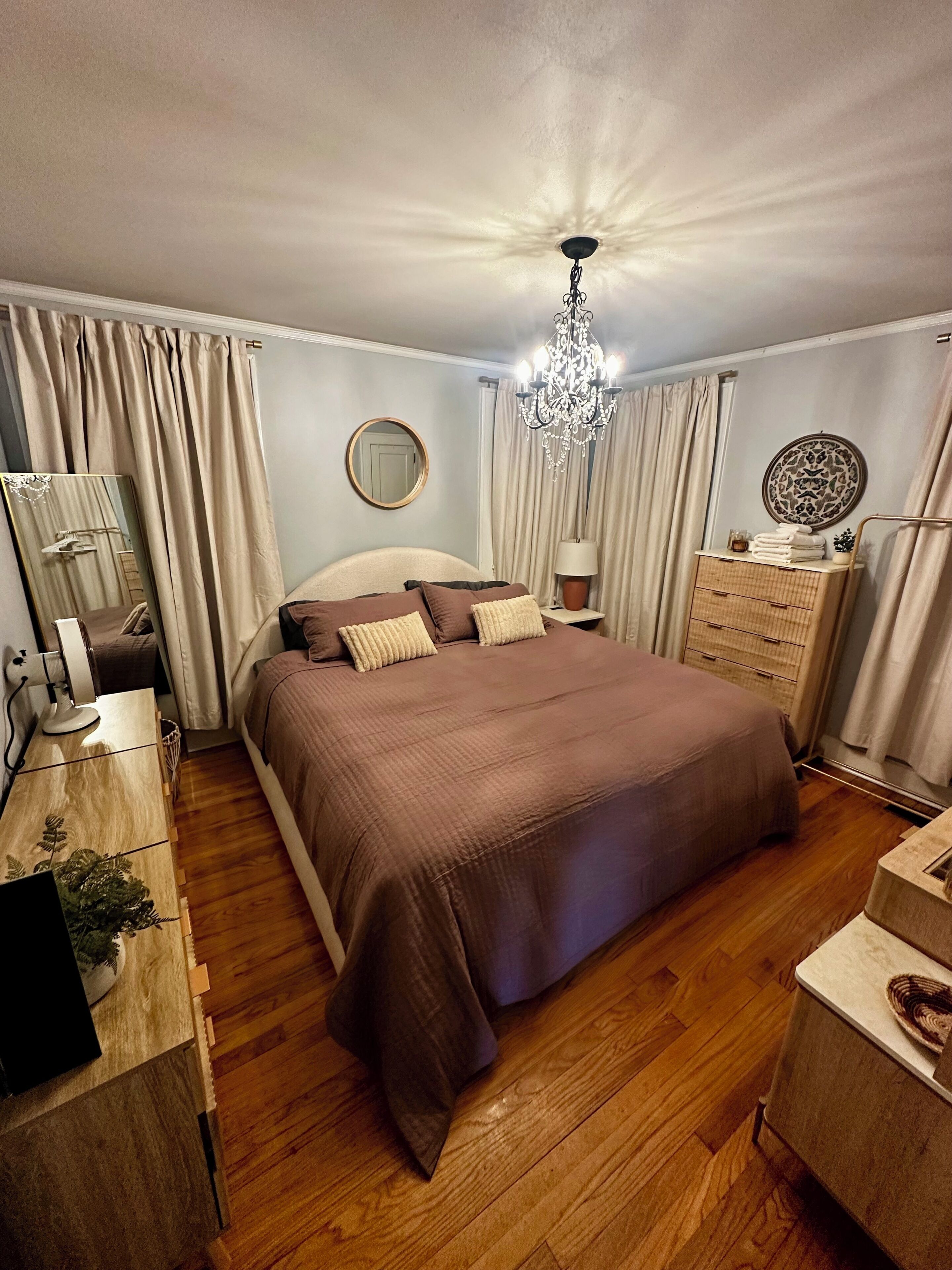 Quarto com cama grande, cómoda de madeira, mesa de cabeceira e um candelabro.