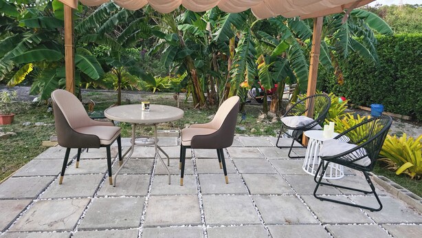 Eine Terrassengruppe im Freien mit rundem Tisch und zwei Stühlen, umgeben von Steinplatten und einer Markise mit Lichterketten.