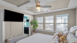 Ein modernes Schlafzimmer mit einem großen Bett, einem Deckenventilator und einem an der Wand befestigten Fernseher.