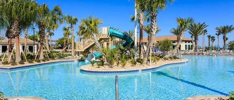 A swimming pool with a water slide, palm trees, and a building with a red roof.