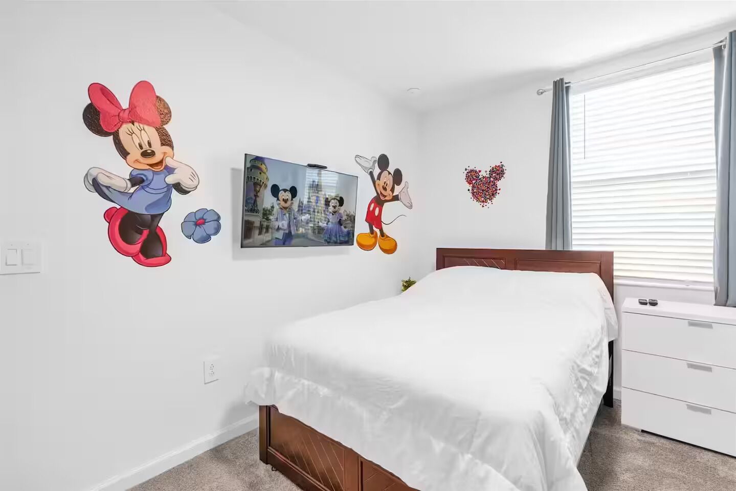 A bedroom with a bed, a dresser, and wall decorations including Mickey Mouse and a heart.