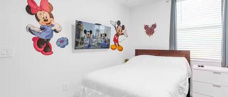A bedroom with a bed, a dresser, and wall decorations including Mickey Mouse and a heart.
