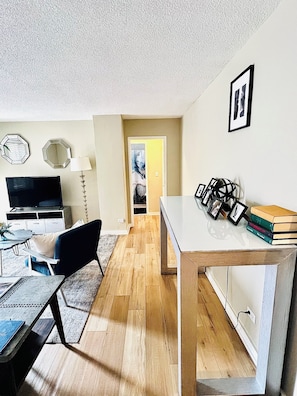 Un salon moderne avec un téléviseur à écran plat, un fauteuil noir, une table basse et une bibliothèque.