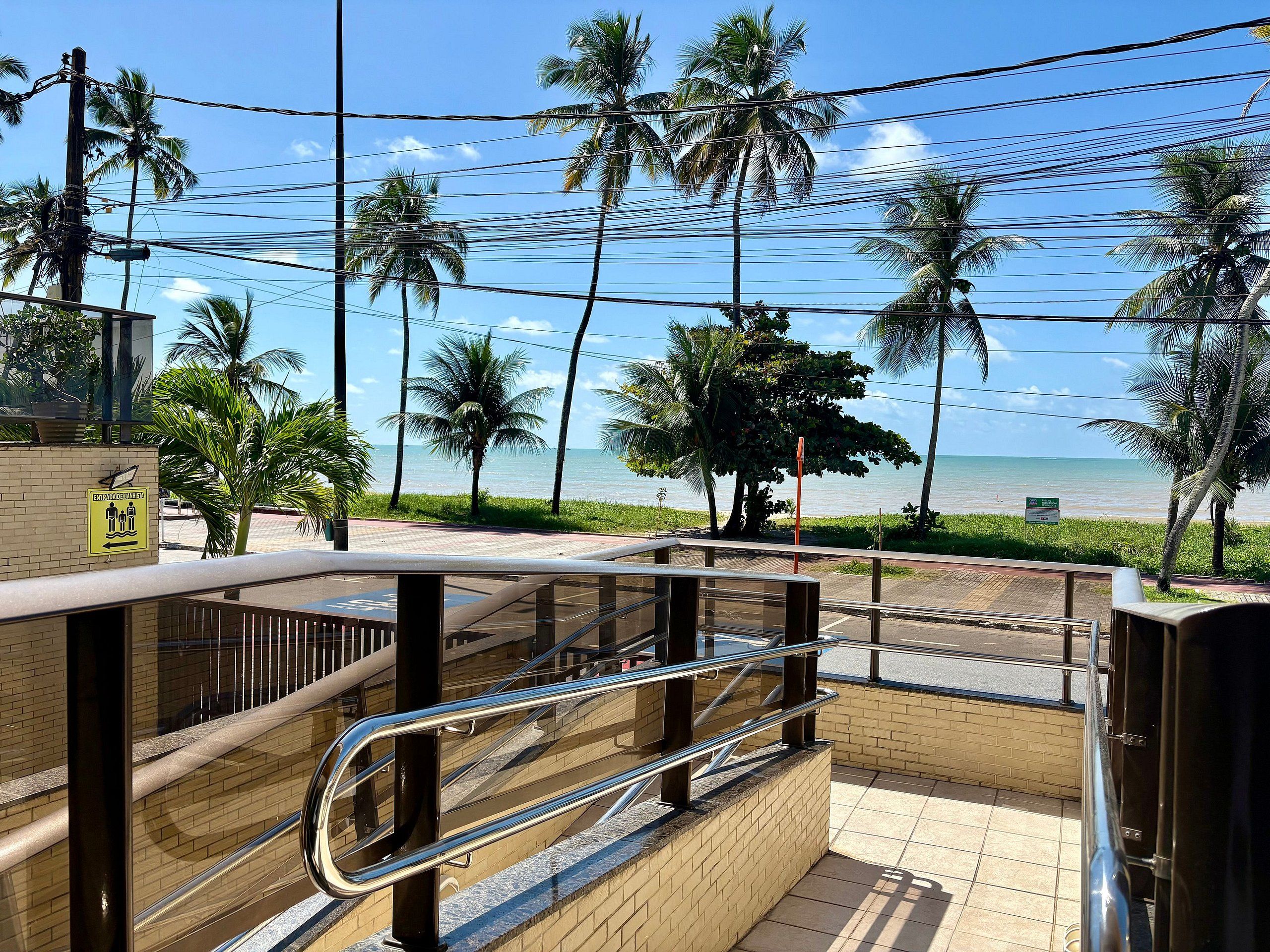 Une vue depuis un balcon donnant sur une plage bordée de palmiers, sous un ciel dégagé.