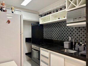 A modern kitchen with a black tiled backsplash, stainless steel appliances, and white cabinetry. - Boulevard Beira mar do Cabo Branco (João Pessoa)
