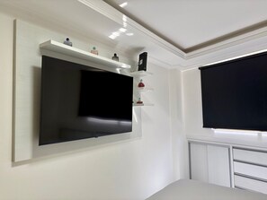 A modern room with a large flat-screen TV mounted on the wall, a white radiator, and a small shelf with decorative items. - Boulevard Beira mar do Cabo Branco (João Pessoa)