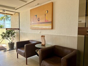 A lobby with two leather armchairs, a glass table, a vase, and a painting on the wall. - Boulevard Beira mar do Cabo Branco (João Pessoa)