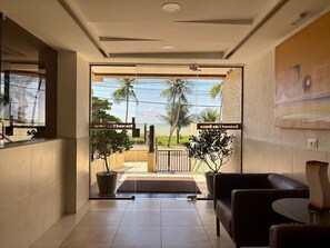 A hotel lobby with a reception desk, a seating area, and a view of palm trees and the sea. - Boulevard Beira mar do Cabo Branco (João Pessoa)