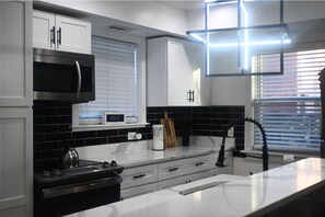 A modern kitchen with white cabinets, a stainless steel microwave, and a kettle on the stove. - Hillcrest Haven • 2BR Home (Washington)