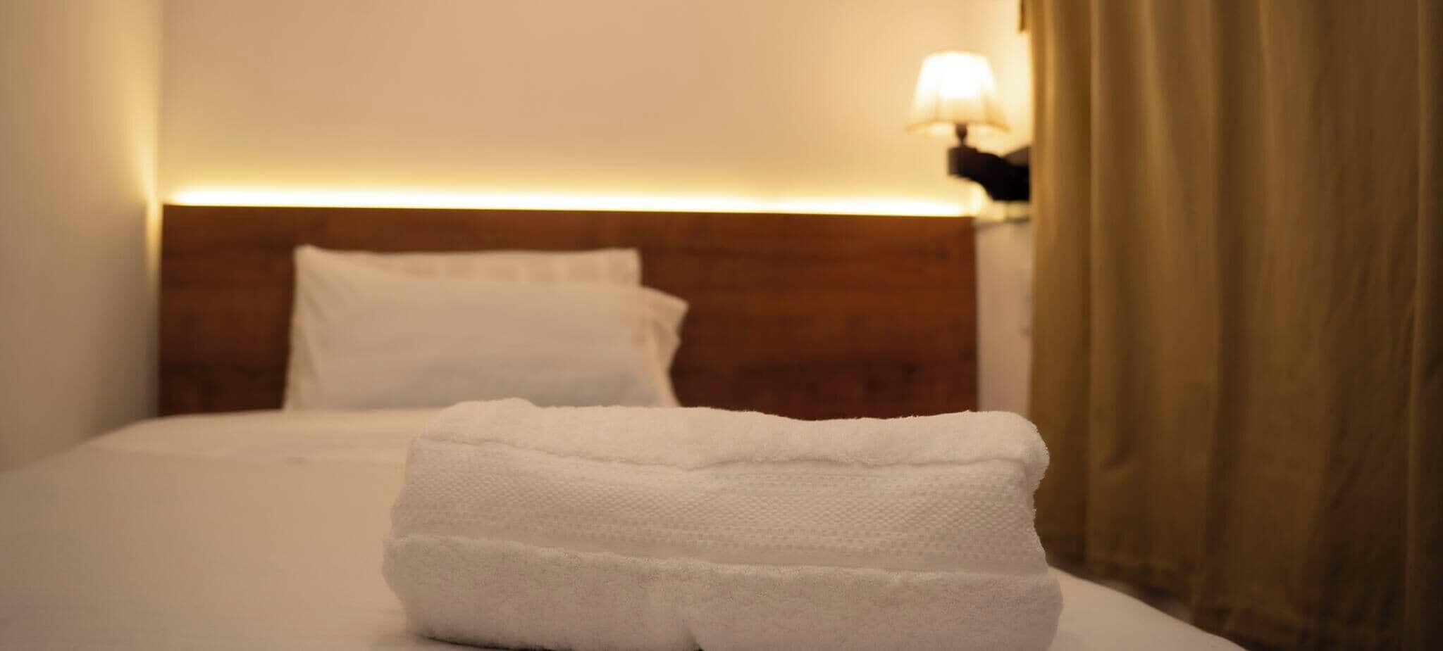 A neatly made bed with white linens and a folded towel in front.