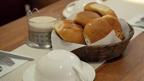A dining table with a basket of rolls, a cup of coffee, and a glass of milk. - Hostal KoryWasy (Uyuni)