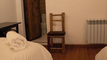 A bedroom with two beds, a wooden chair, a radiator, and a table with a towel.