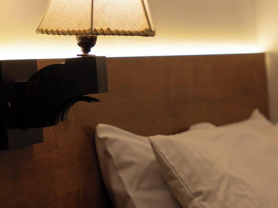 Una lámpara de pared con pantalla de tela, un cabecero de madera y una almohada blanca sobre una cama.