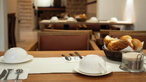A dining table set with white plates, bowls, and a teapot, with bread and a basket in the background. - Hostal KoryWasy (Uyuni)