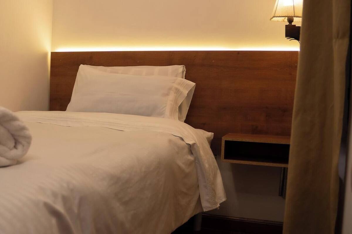 A neatly made bed with a rolled towel, a wooden headboard, and a bedside table with a lamp.