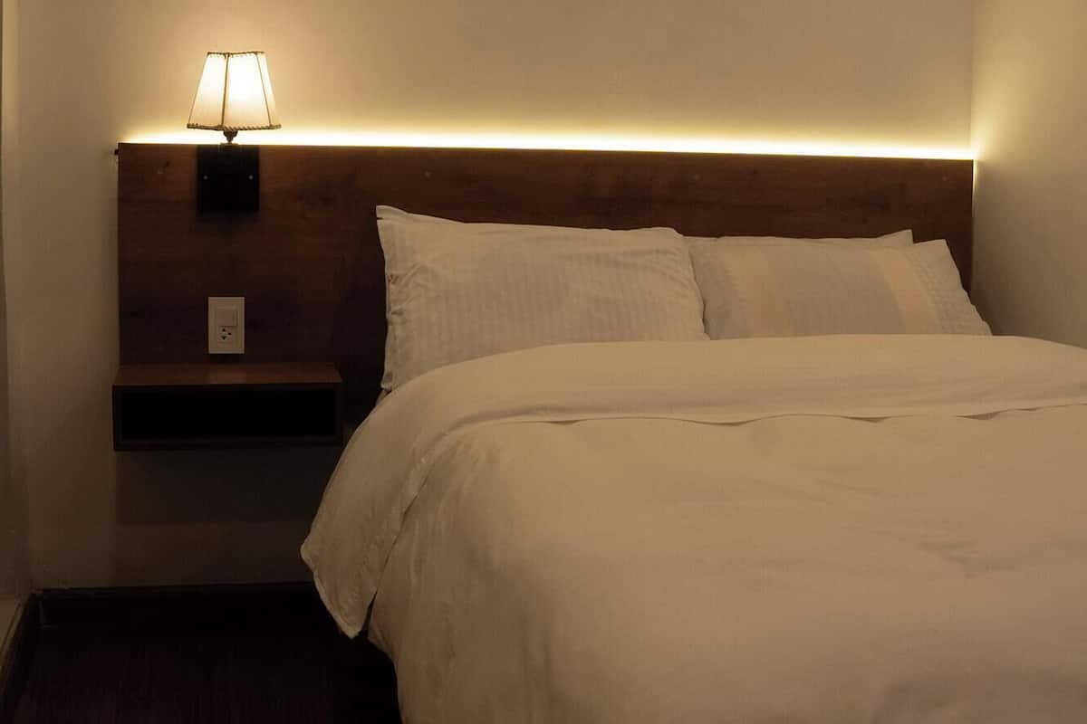 A hotel room with a neatly made bed, a bedside lamp, and a nightstand.
