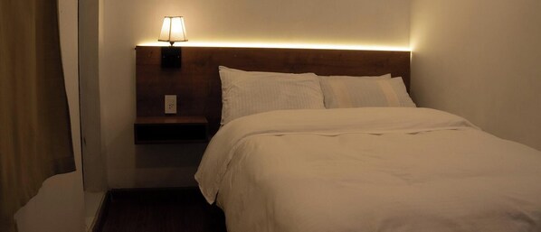A hotel room with a neatly made bed, a bedside lamp, and a nightstand.