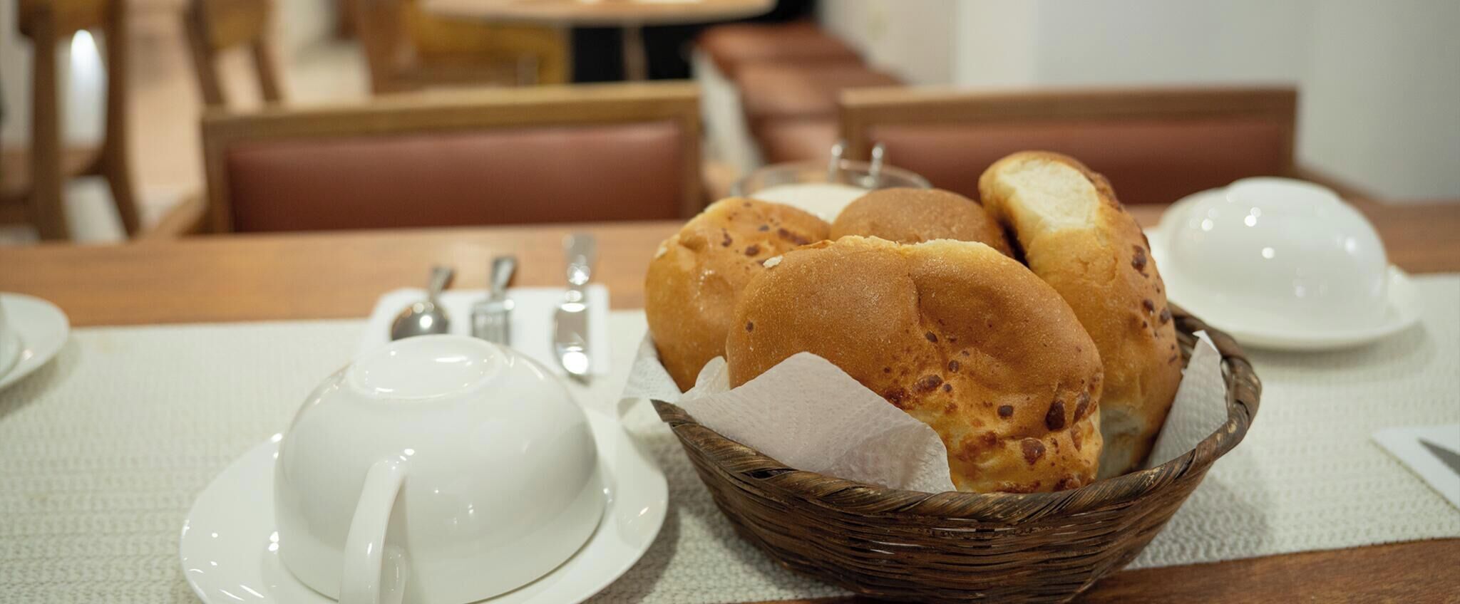 Une table à manger avec un panier de petits pains, une théière et une tasse.