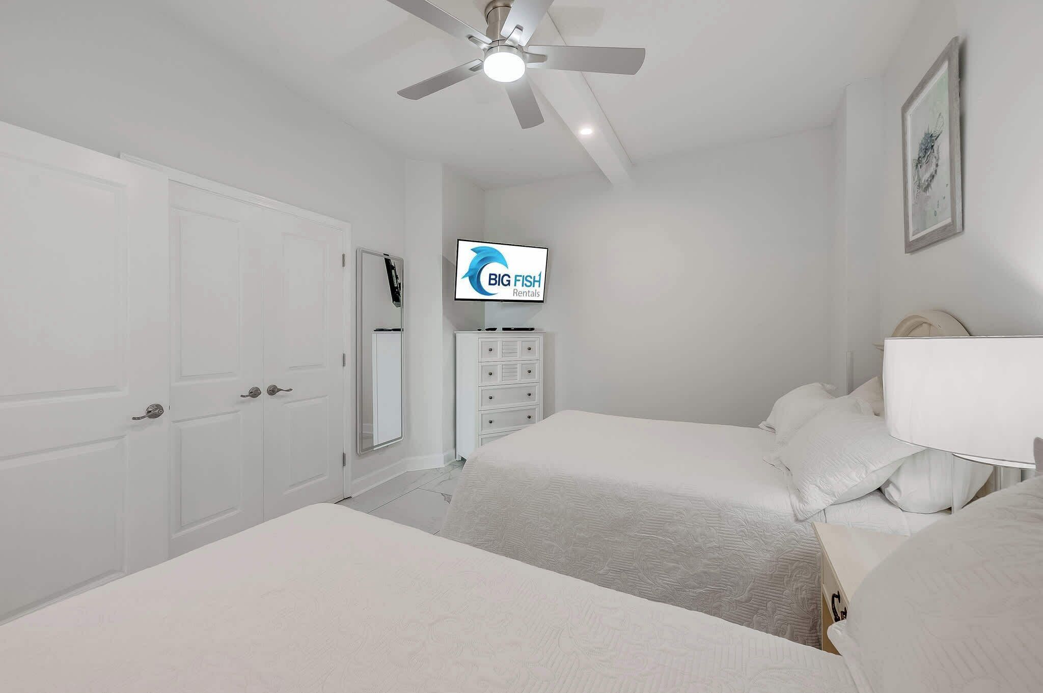 A bedroom with two beds, a ceiling fan, a TV, and a dresser.