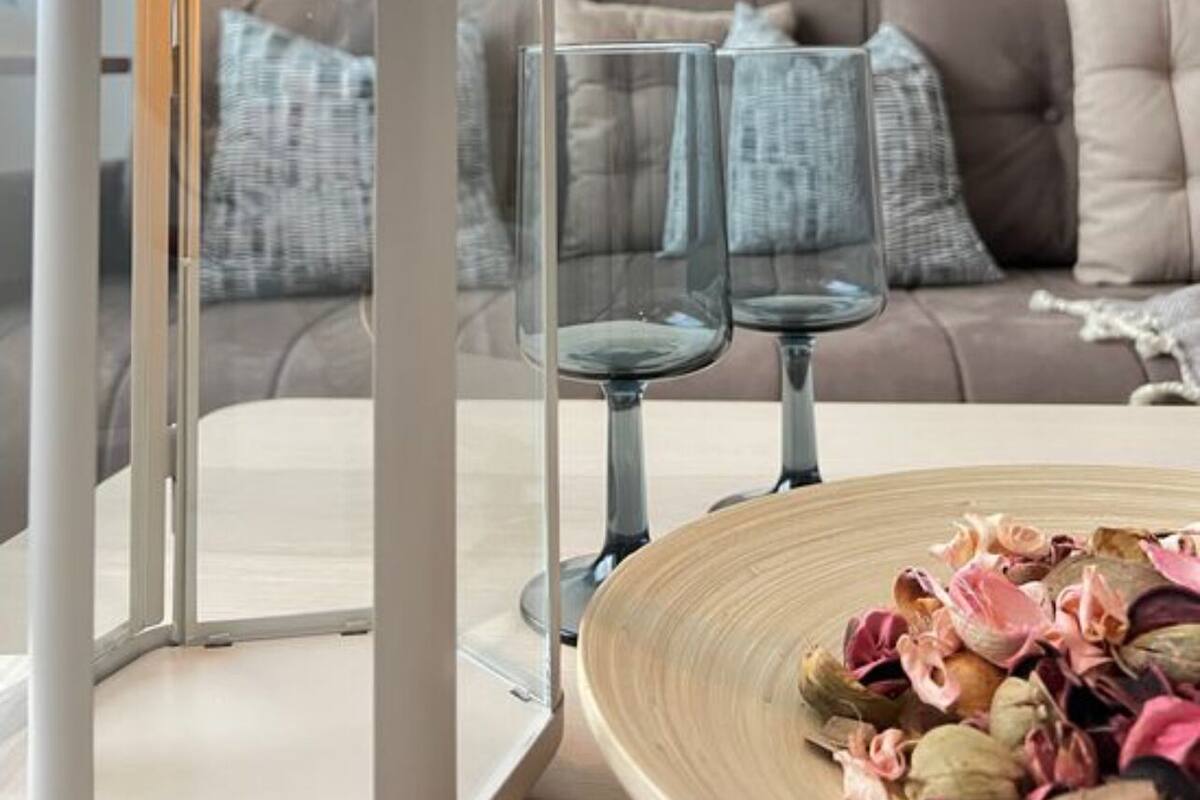 Uma sala de estar moderna com um sofá branco, uma mesa de centro de vidro e um candeeiro decorativo.