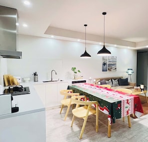 Una cocina moderna con armarios blancos, una mesa de comedor con mantel festivo y lámparas colgantes.